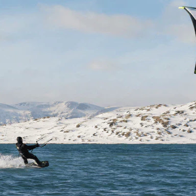 A rider enjoys kite kitesurfing across cold blue water beside snow-covered mountains beneath a large airborne kite