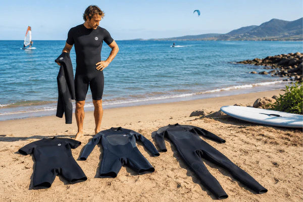 A man compares different wetsuit for men options on a sunny beach before choosing one for summer water sports