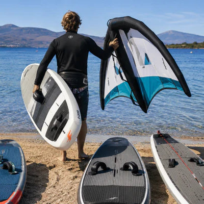 This realistic photo shows a rider choosing a wing foil board from several options on a beach before entering the water